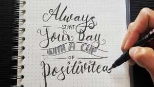 Someone writes in a bullet journal the phrase, ”Always start your day with a cup of positivitea.”