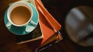 A teal cup of coffee sits on a stack of journals.