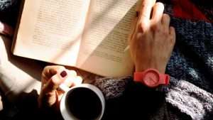Someone holds a cup of coffee while holding a book in their lap.