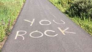 The words, “You Rock” are spray-painted on a sidewalk with grass on either side.