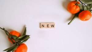 Two branches with two oranges on each are placed in the top right and bottom left corners, with the word “New” spelled out on wood letter tiles.