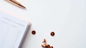 A rose gold pen and rose gold push pins next to a pink yearly planner.