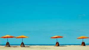 Four umbrellas on a beach, with two red folding chairs under each.